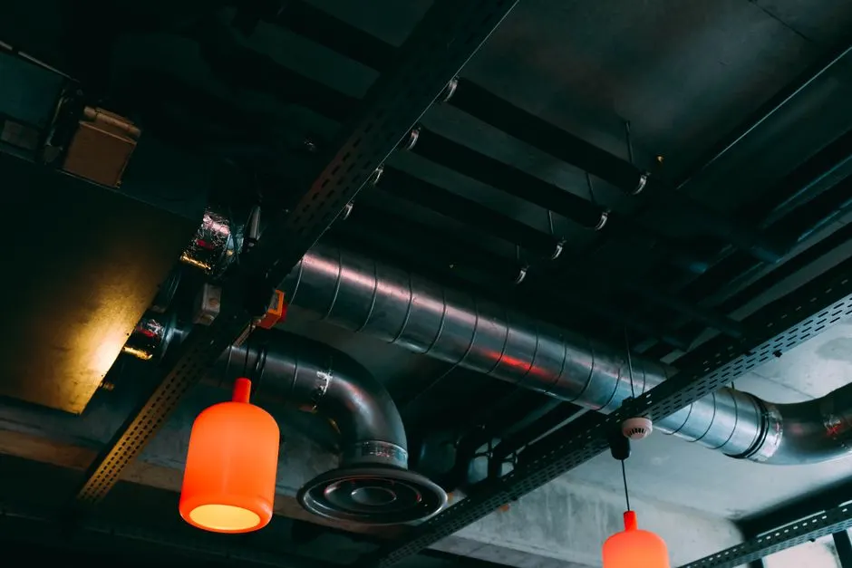 Low-angle view of a modern industrial ceiling featuring ducts and red lamps.